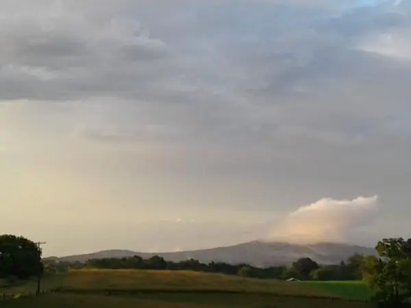 Storm clouds and a wisp of low cloud over a distant mountain beyond a hayfield