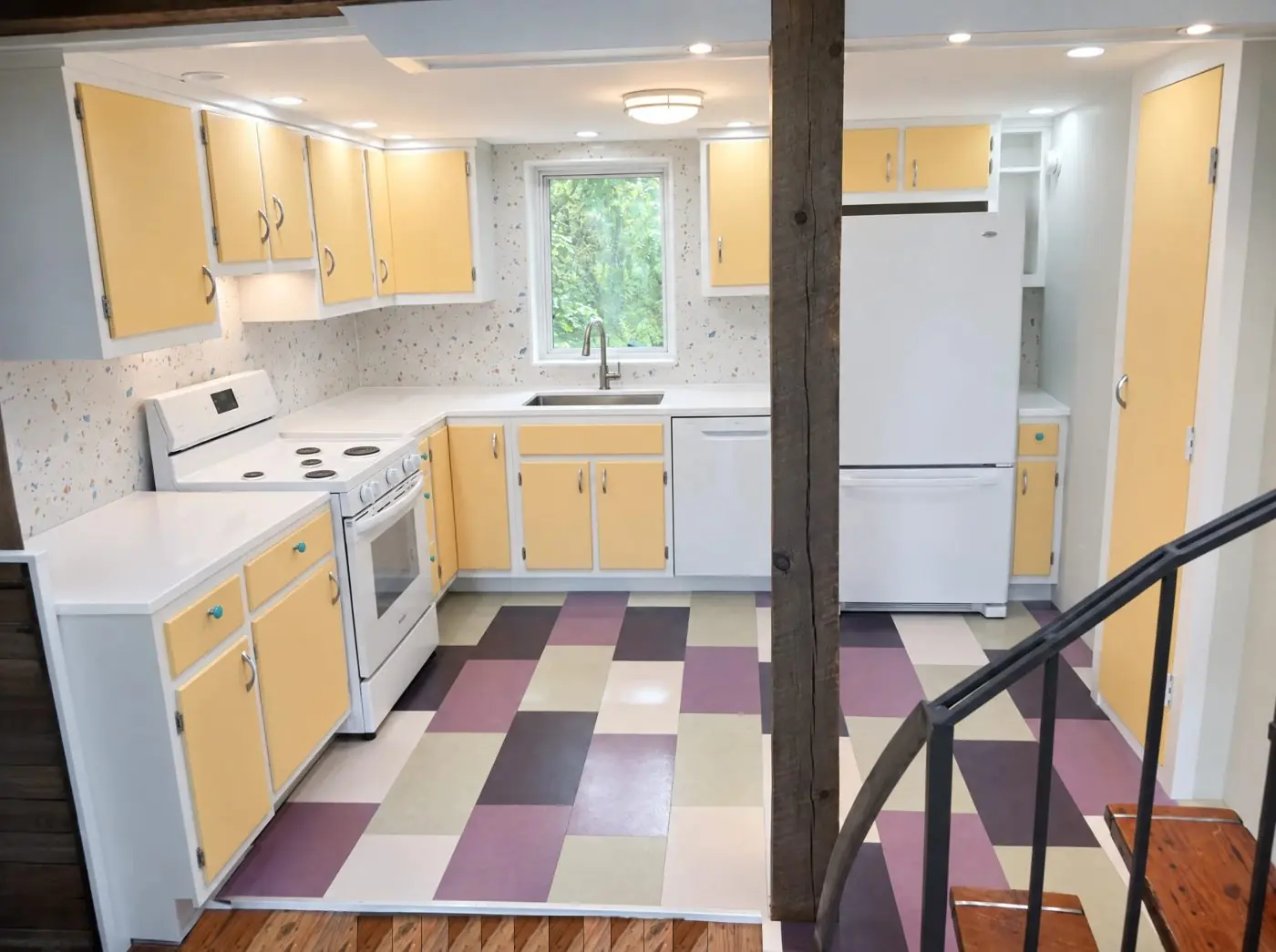 The kitchen with yellow cabinets, white countertops and a violet and mint checkerboard cork floor