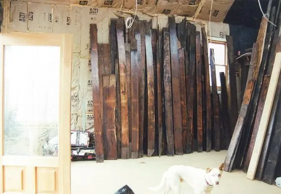 Reclaimed antique boards stacked upright against the wall of the house during the rebuild, with a white dog in the foreground