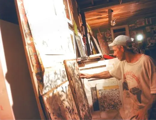 The artist reaching toward charcoal drawings leaning against the wall of his studio