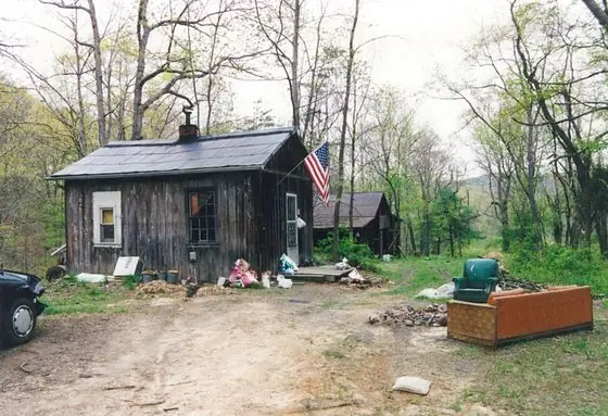 The schoolhouse around 2001, a weathered board-and-batten cabin with a flag and a chimney