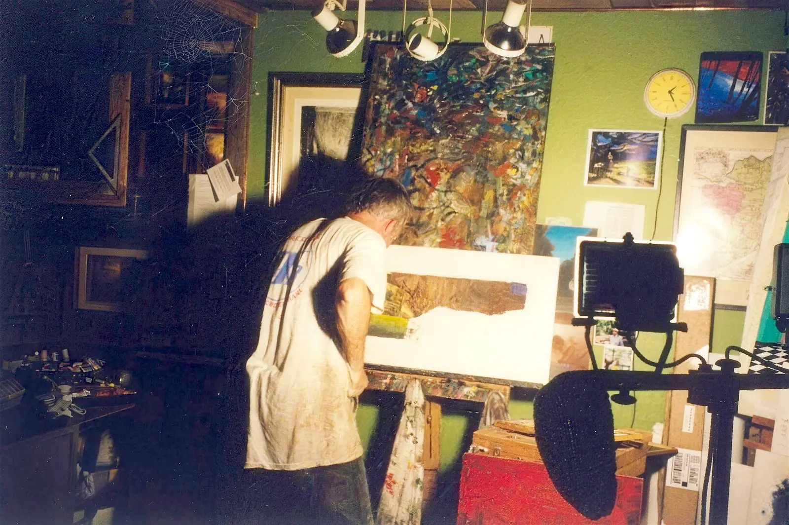 The artist at his easel in the green studio, working on a large painting under track lights