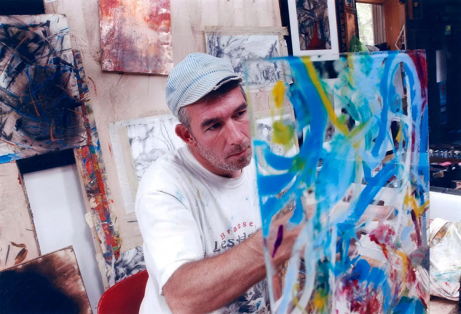 The artist at work in his studio, brush in hand before a large canvas of swirling blue, yellow and white strokes