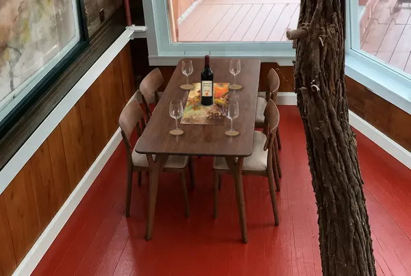 Serving suggestion. The dining table set with a placemat, a bottle of wine and four glasses beside the porch window, with cork coasters and a placemat patterned with one of Pete Kephart’s paintings, photo 30 of 32